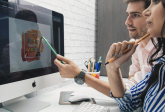 Principales tendances du design graphique aux États-Unis de mai 2023 à mai 2024&nbsp;: étude sur les tendances de l'IA et de Google (780 x 780). Ordinateur iMac avec conception graphique à l'écran. Clavier, souris, tapis de souris et porte-stylo. Homme en chemise rose et femme en chemise rayée bleue et blanche. Écran de visualisation.