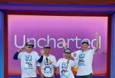 Quatre membres de Markzware L'équipe, vêtue de t-shirts et de casquettes assortis aux couleurs de la marque, se tient debout, souriante et le pouce levé, sous les couleurs vives violettes et roses.Canva Entrée de l'événement « Create » 2025, sur laquelle on peut lire « Inexploré ».