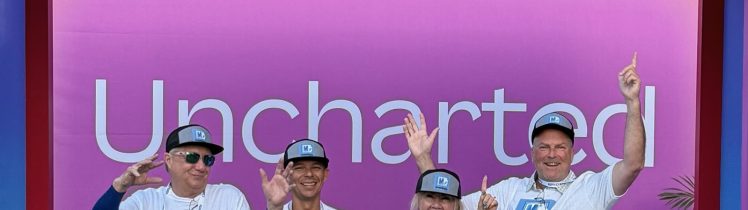 Four members of the Markzware team wearing matching branded t-shirts and hats stand smiling with thumbs up under the vibrant purple and pink “Canva Create” 2025 event entrance, which reads “Uncharted.”